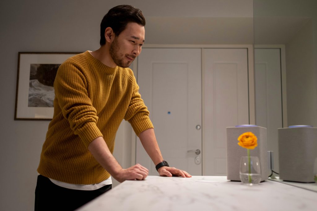 Man wearing an orange jumper talking to smart speaker