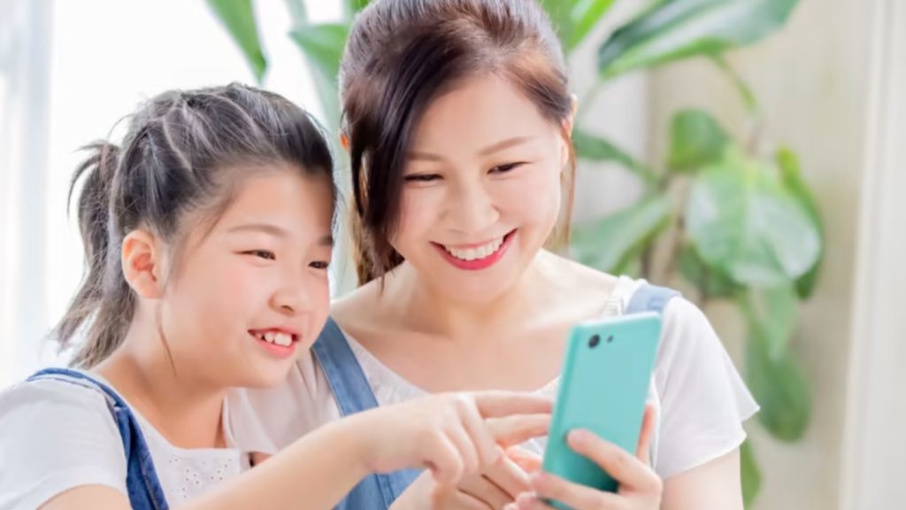 Un enfant et sa mère regardent TikTok sur un téléphone intelligent ensemble. Il est important de discuter avec les jeunes à propos de la sécurité sur internet.