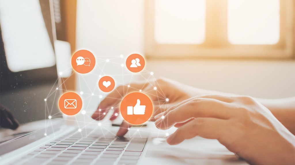Une personne tape sur un clavier d'ordinateur. Des icônes de like, de commentaires et de partages sont illustrés au-dessus des mains.
