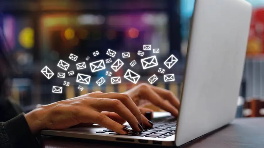 Background with hands typing on a laptop keyboard and digital envelope icons floating above symbolizing outgoing emails and email marketing.