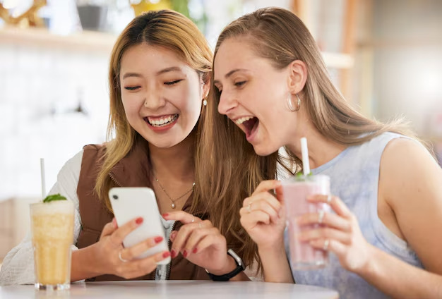 deux femmes rient à cause du vidéo TikTok qu'elles voient sur leur téléphone intélligent. Elles sont atteintes par le marketing humoristique