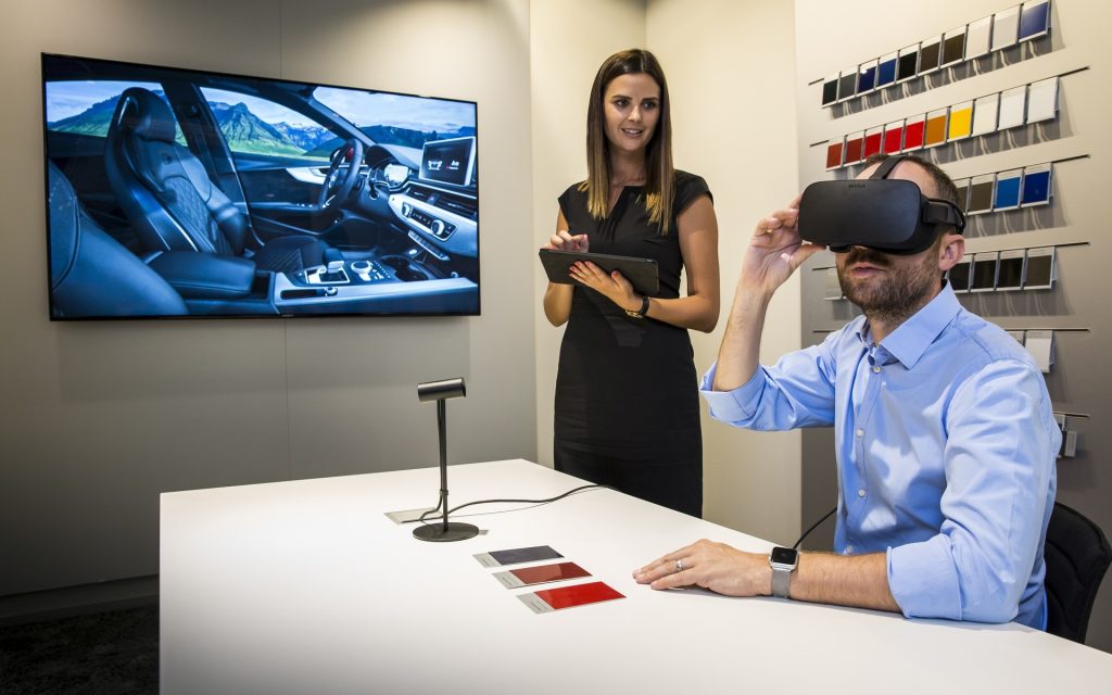 Un homme portant un casque de réalité virtuelle dans une concession Audi, explorant la personnalisation de son véhicule, assisté par une conseillère.