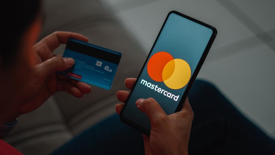 A person holding on the left hand a card and on the right hand a phone screening mastercard