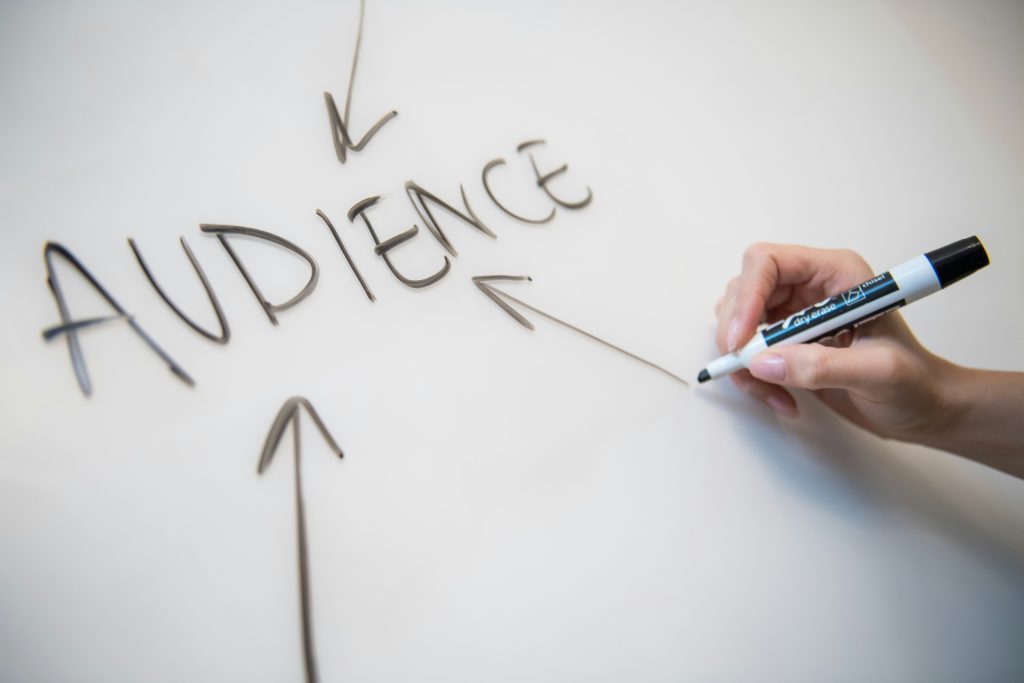 Whiteboard with AUDIENCE written of it with arrows pointing to the word. Hand with black marker completing the third arrow.