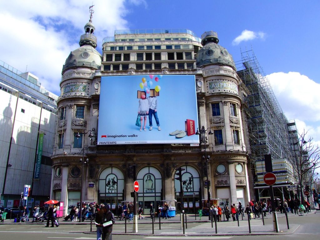 Un énorme panneau numérique sur un bâtiment à Paris affiche une annonce de Camper indiquant "imagination walks"