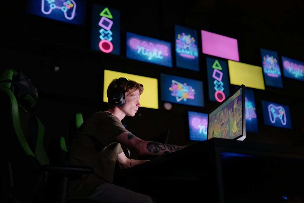 Un garçon joue à un jeu vidéo dans une salle sombre devant des panneaux numériques colorés