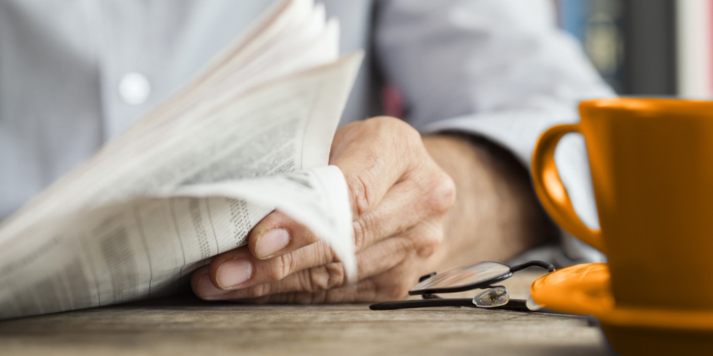 Older man reading a traditional newspaper with a cup of coffee on the table, symbolizing outdated media consumption habits compared to Gen Z's digital preferences