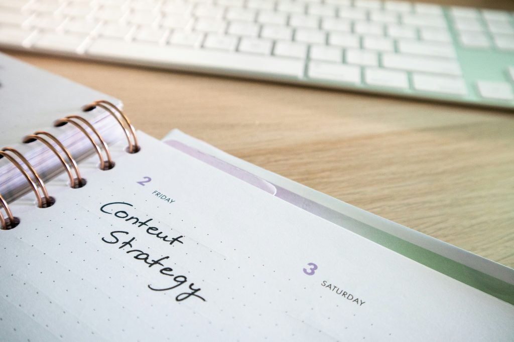 Weekly planner agenda with Content Strategy written on it. Keyboard visible in background on wooden table.