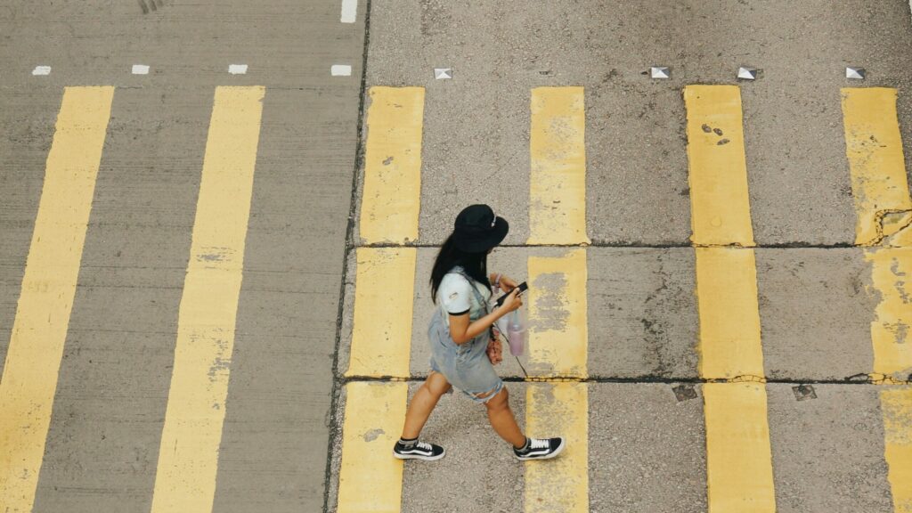 Woman walking on a crossway looking down at her phone. Source : https://unsplash.com/photos/woman-walking-on-pedestrian-lane-PDHwGhByXOM