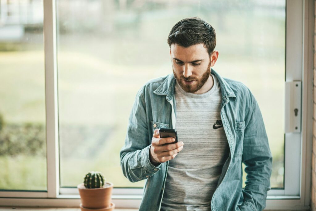 Man looking at his phone, Source: https://unsplash.com/photos/man-holding-a-smartphone-near-the-window-J2e34-1CVVs