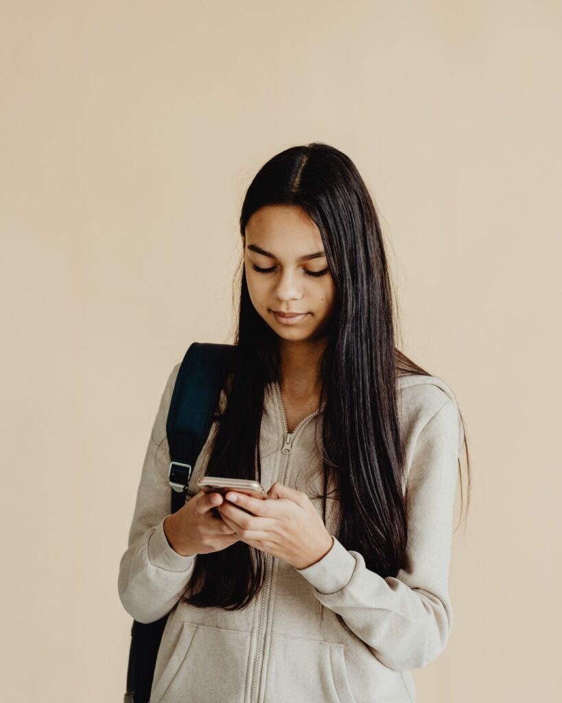Une jeune fille debout avec un sac à dos noir regarde son téléphone d'un visage neutre, illustrant la consommation passive de contenus dans une bulle de filtres.