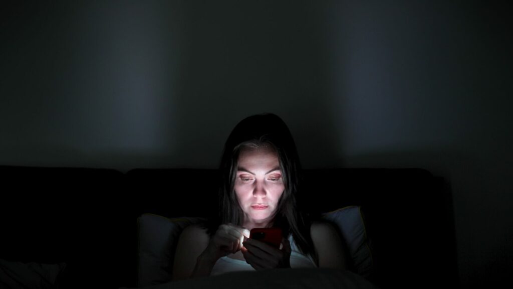 Une jeune femme allongé dans son lit regarde son téléphone avec un regard perdu, illustrant l'isolement causé par une bulle de filtres et les algorithmes de recommandation.